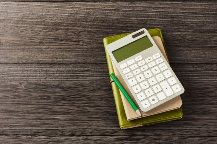 A calculator and pencil rest on notebooks on a desk.