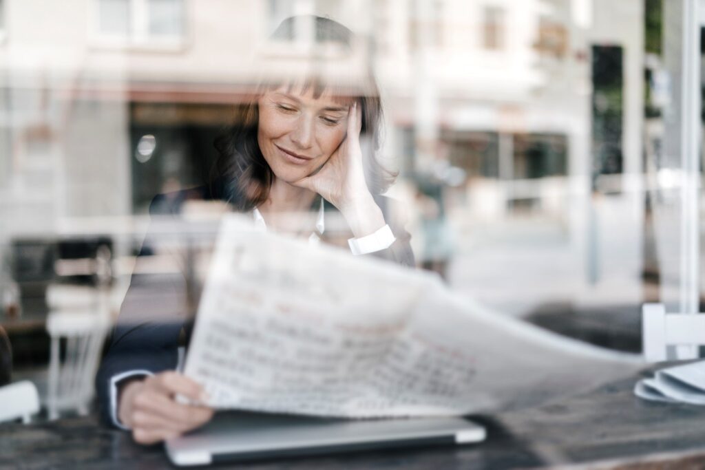 Woman reading newspaper at café window.