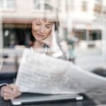 Woman reading newspaper at café window.